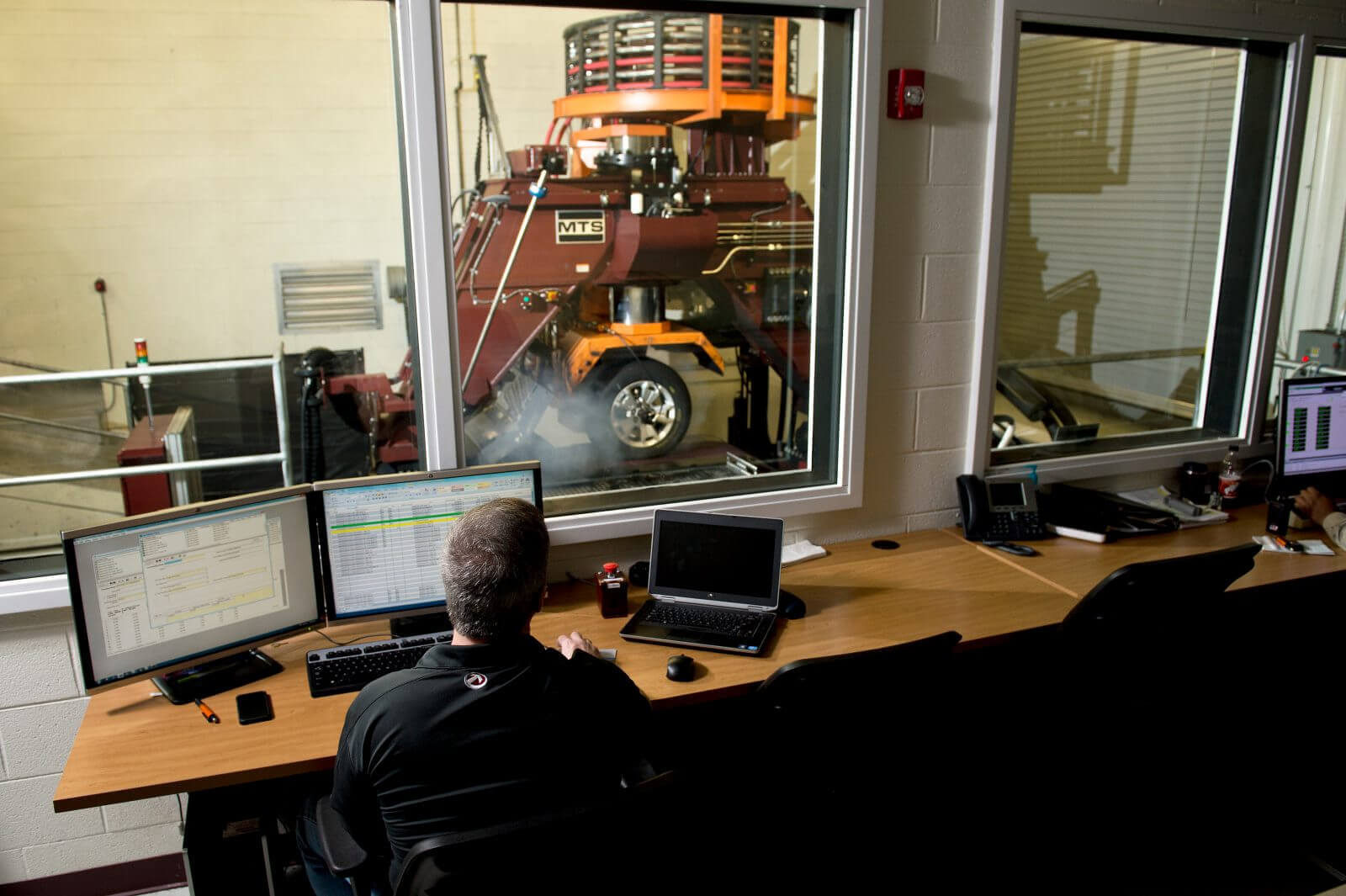 A person sitting behind a computer screen watching an indoor tire testing machine
