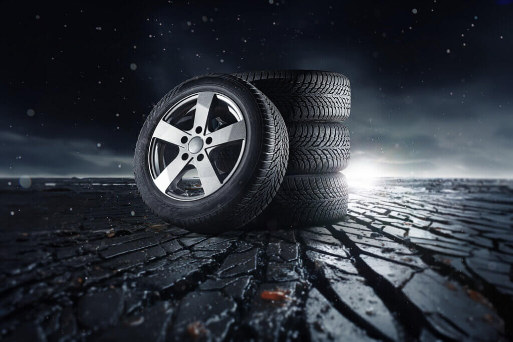 Four car tires on a cracked surface under a dark, dramatic sky, one standing upright and three stacked behind it.